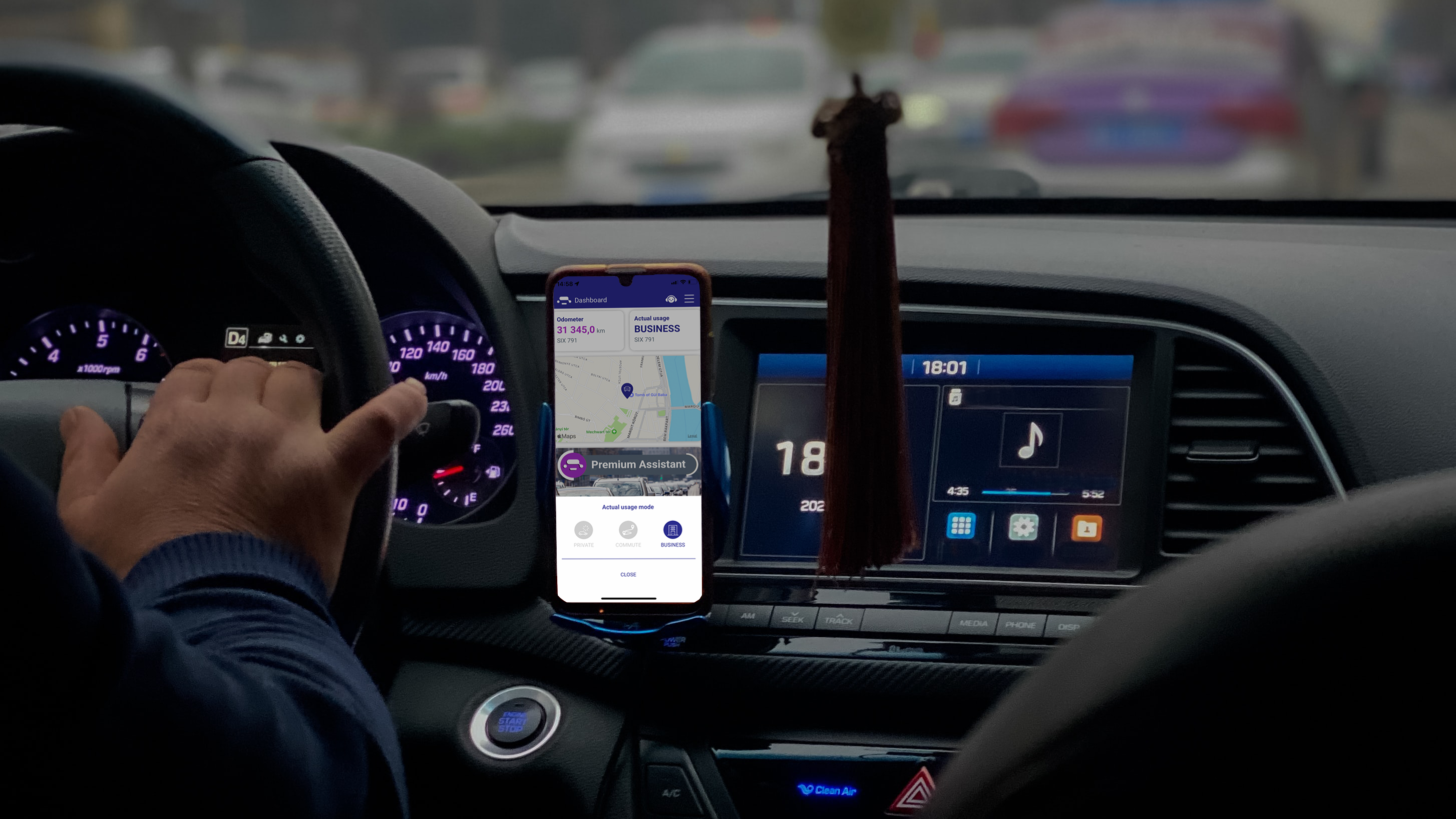 Interior of a car with the driving wheel, and a mobile phone (fixed to the dashboard) with Urbaniqe app on the screen