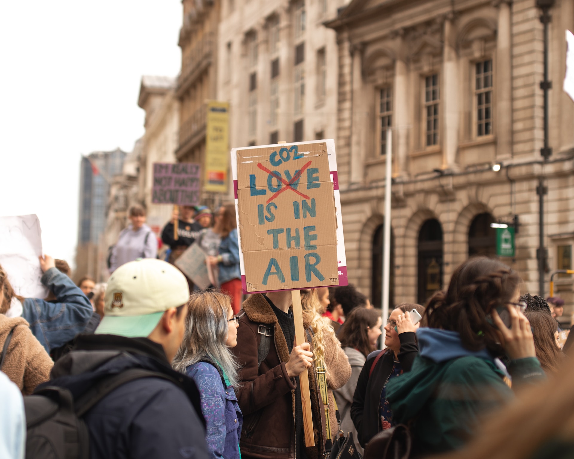 activist in a demonstration holds a carboard paper plate with the words love is in the air, where there is a big red x through the word love, and CO2 is added above it instead